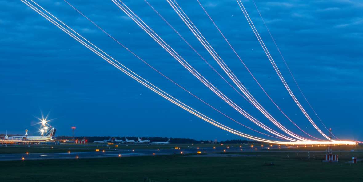 Air traffic at an airport The photo was taken in long exposure and shows an airport. The lights of the planes taking off and landing leave glowing streaks in the dark sky.